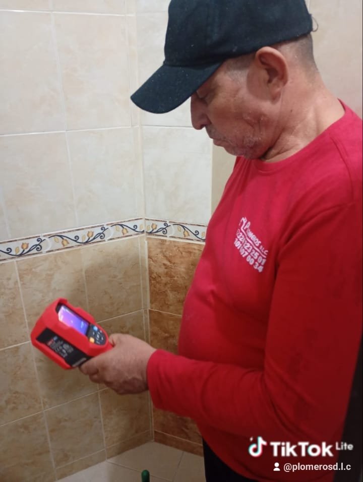 Manos de un plomero experimentado sosteniendo una llave de tubo junto a herramientas y accesorios ordenados